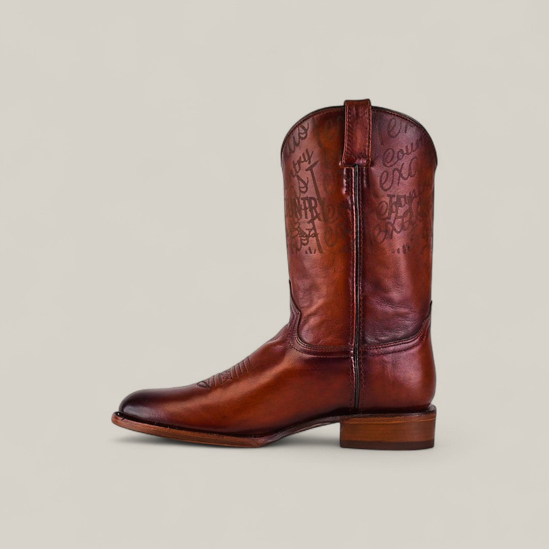 The Wyatt - Camel - Roper Toe is a single brown cowhide boot with a low heel, decorative stitching, and engraved writing on the shaft, shown in profile against a light background, showcasing premium leather craftsmanship.