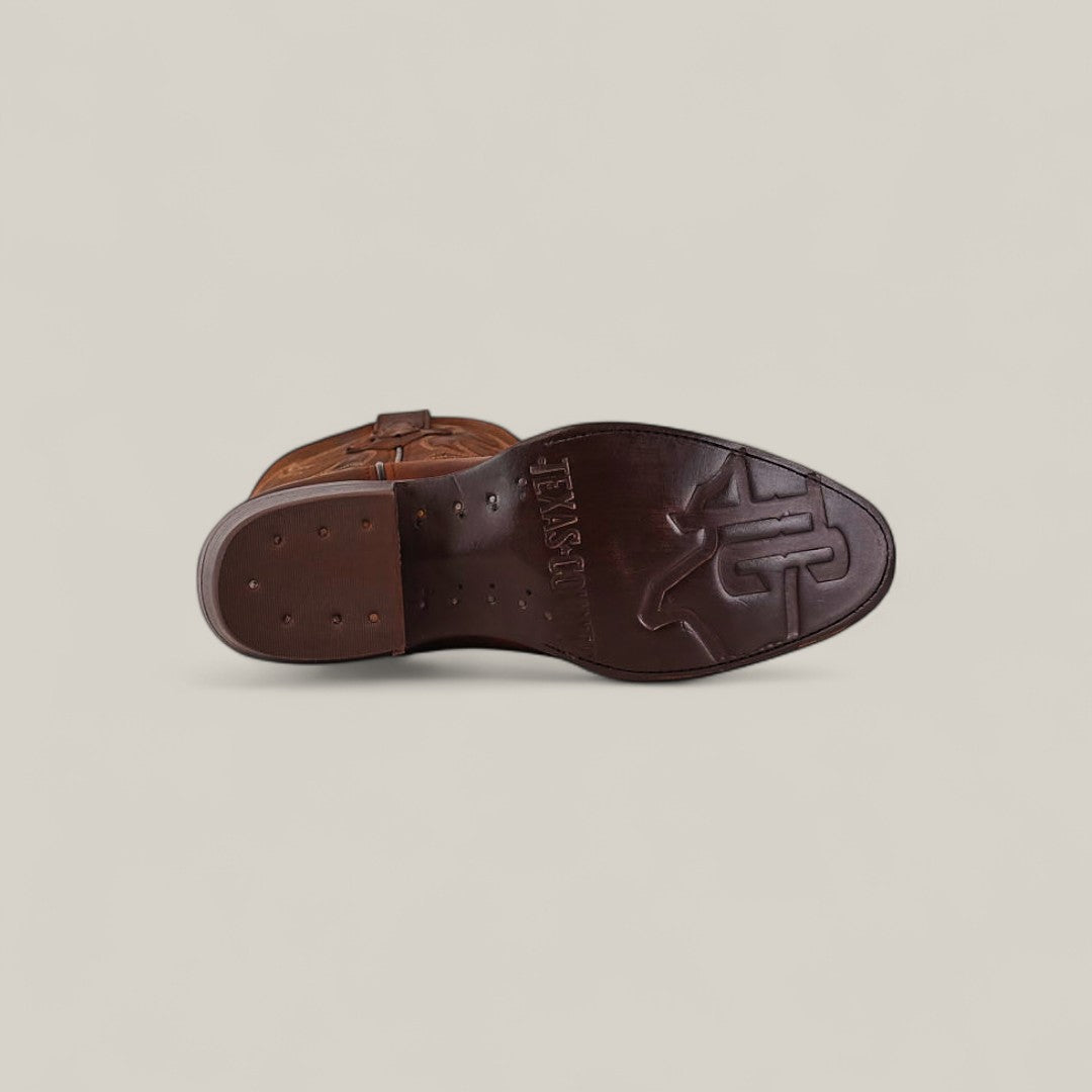 The image displays the sole of the Dutton - Brick - Roper Toe boot, crafted from brown cowhide. It features embossed patterns, MEXICO, and a large star design, set against a plain light beige background.