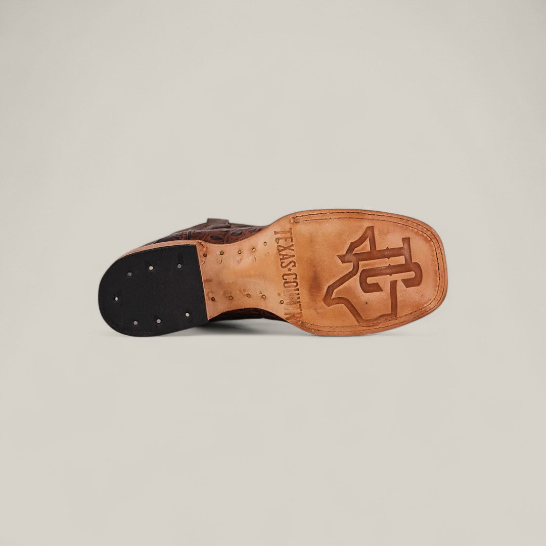 The image shows the sole of the Jonh - Brown - Square Toe premium leather boot with the Texas A&M University logo and TEXAS.COM engraved on tan leather. The dark heel features metal tacks, showcasing quality craftsmanship throughout.