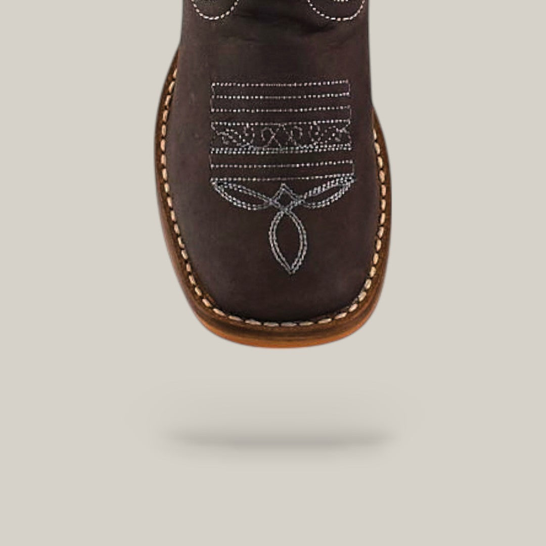 A close-up of the toe of the Orion Suede Oxford - Square Toe Kids Boot in dark brown, featuring white decorative stitching and a light brown welt, set against a plain beige background.