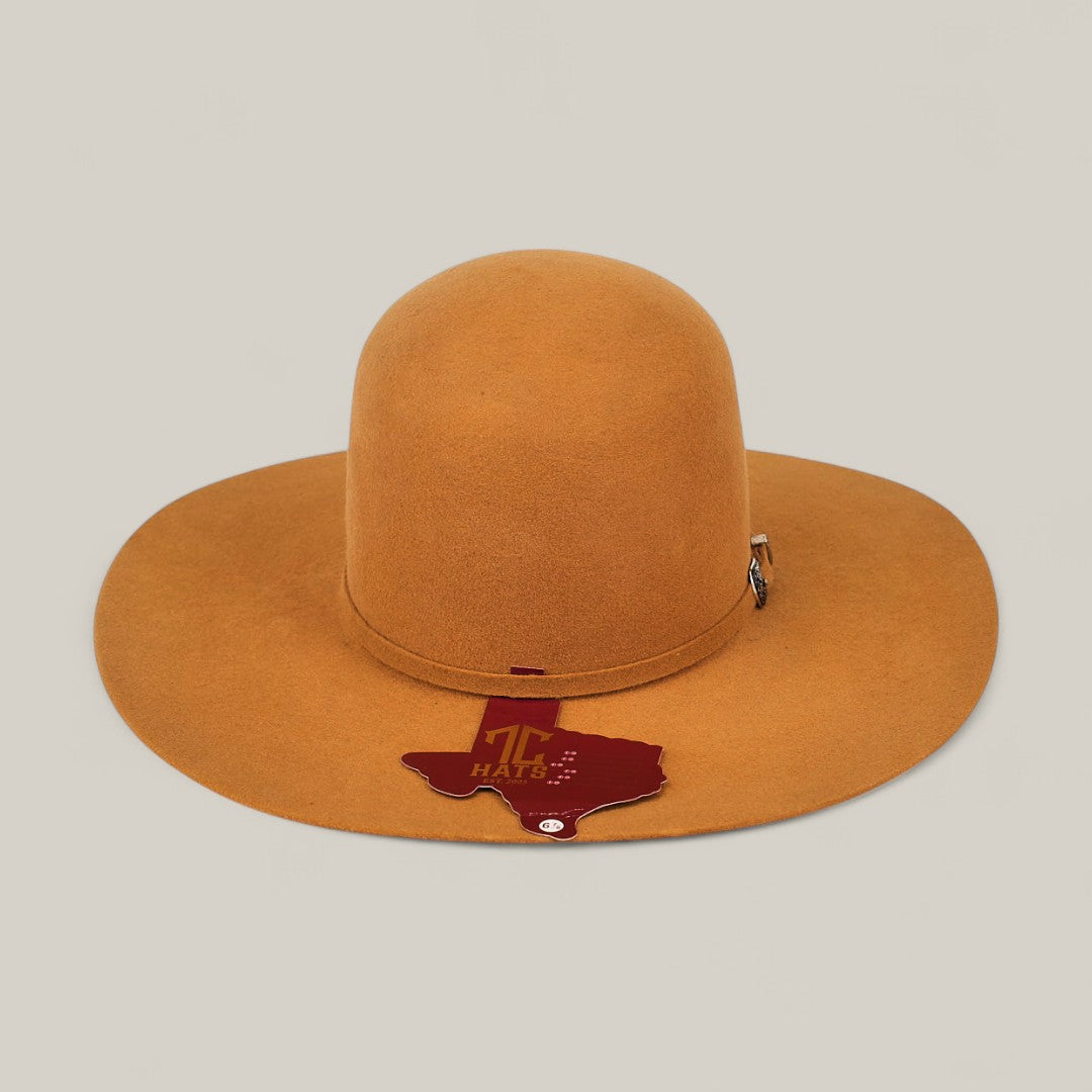 The 4X Caramel - TC Hats features a wide brim, camel color, open crown, decorative band, and a brown Texas-shaped tag on the brim, all displayed against a plain light background.