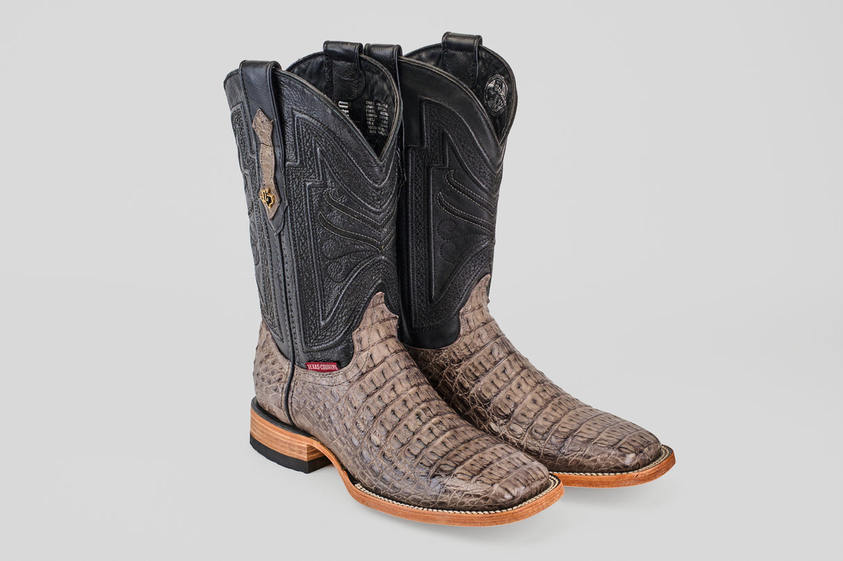 The Exotic Caiman Horn Back - Serpentine - Square Toe boots feature textured brown caiman leather, black shafts with intricate stitching, and wooden soles, displayed on a plain light gray background.