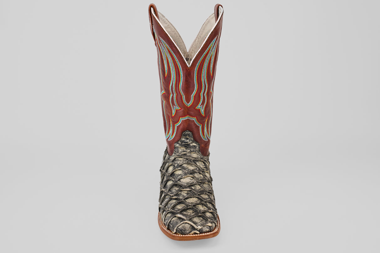 The Robinson - Newspaper - Square Toe is a single cowboy boot featuring a brown and red stitched leather upper and a textured, scaly dark brown Purarucu leather lower, displayed against a light gray background.