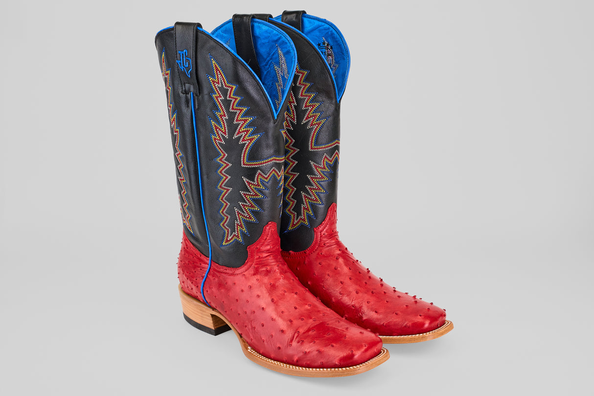 The Crowley - Red - Square Toe cowboy boots feature bright red ostrich leather feet, black shafts with colorful stitching, and blue lining at the top, showcased against a light gray background.