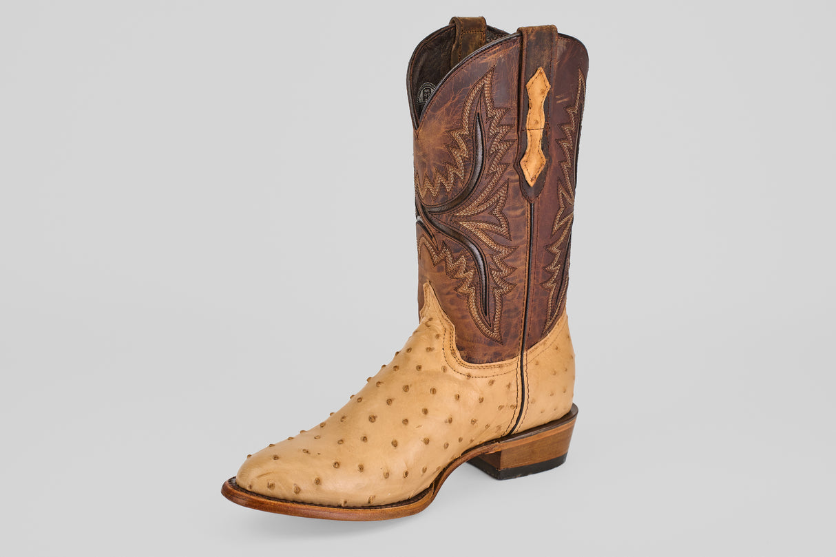 The Exotic Full Quilt Ostrich - Orix - Round Toe is a handcrafted cowboy boot featuring a light tan ostrich leather foot and a dark brown shaft with decorative stitching, shown against a plain light background.