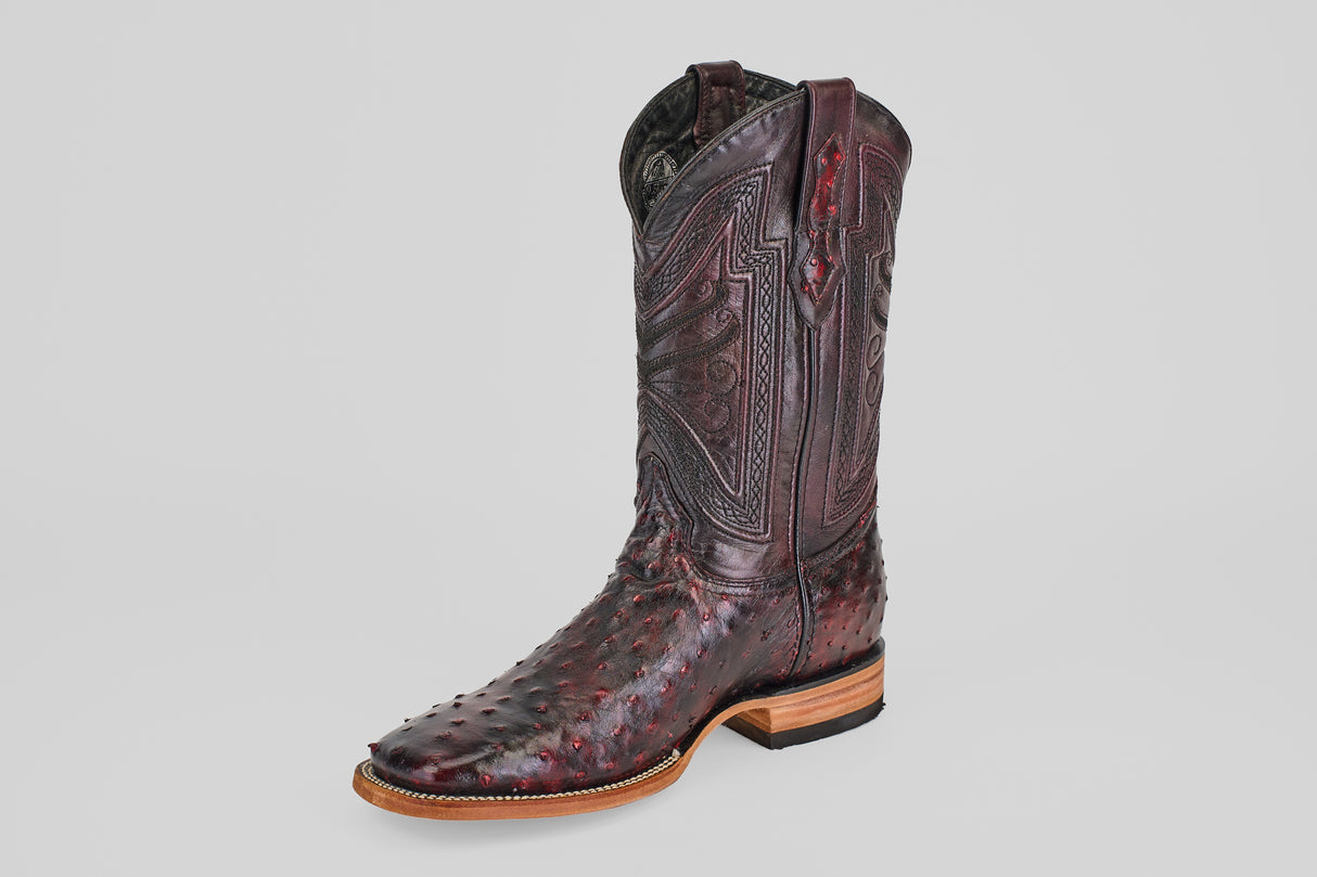 A single Exotic Full Quilt Ostrich boot in Black Cherry with a square toe, featuring intricate shaft stitching and textured ostrich leather, is displayed on a plain gray background.