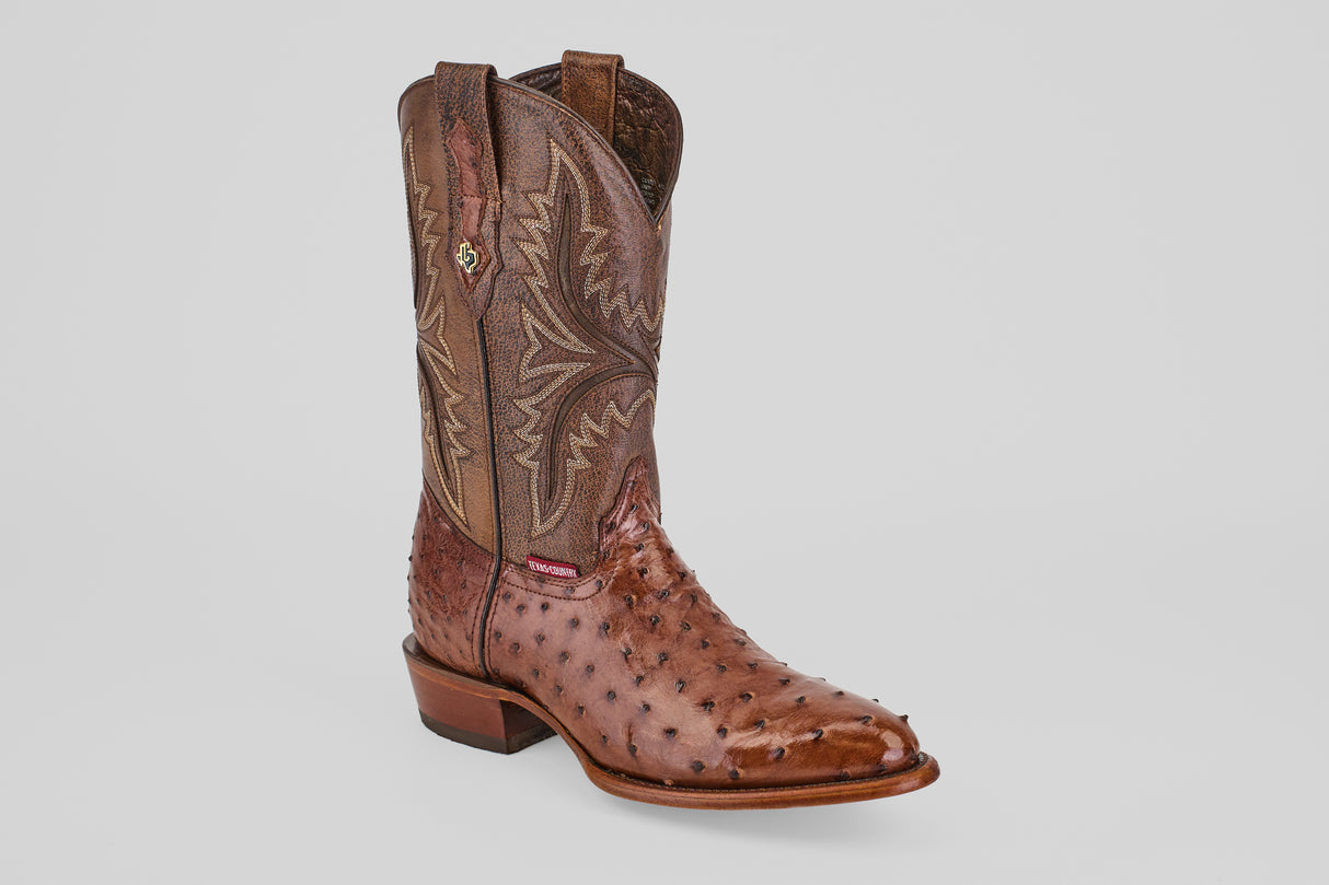 The Austin - Brown - Round Toe cowboy boot features decorative stitching on the shaft and a textured, spotted avestruz pattern on the foot, displayed against a plain light gray background.