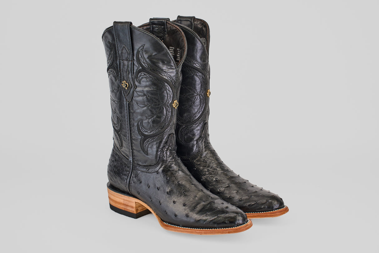 The Austin - Black - Roper Toe boots feature black ostrich leather, decorative stitching, stacked wooden heels, and roper toes, showcased on a plain light gray background.