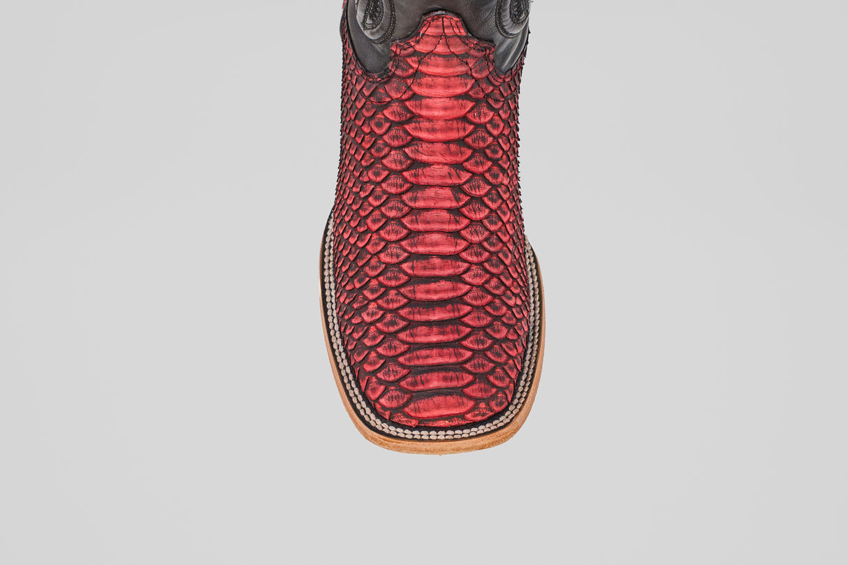 A close-up of the Tanner – Scarlet – Square Toe boot highlights its red python leather, black accents, and square light brown sole, capturing classic western style against a plain white background.