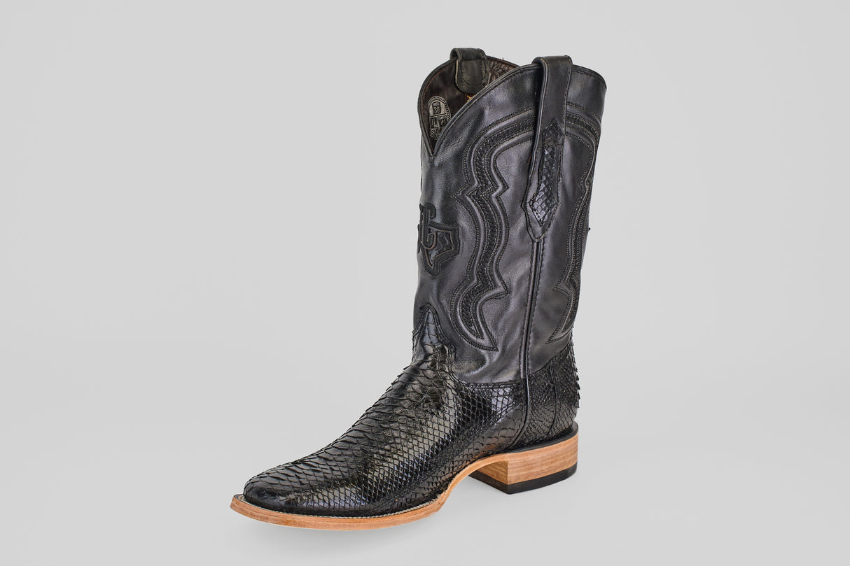 The Tanner - Black - Square Toe boot features a textured snakeskin pattern, intricate stitching on a tall shaft, and a light brown wooden heel and sole, shown against a plain light gray background.