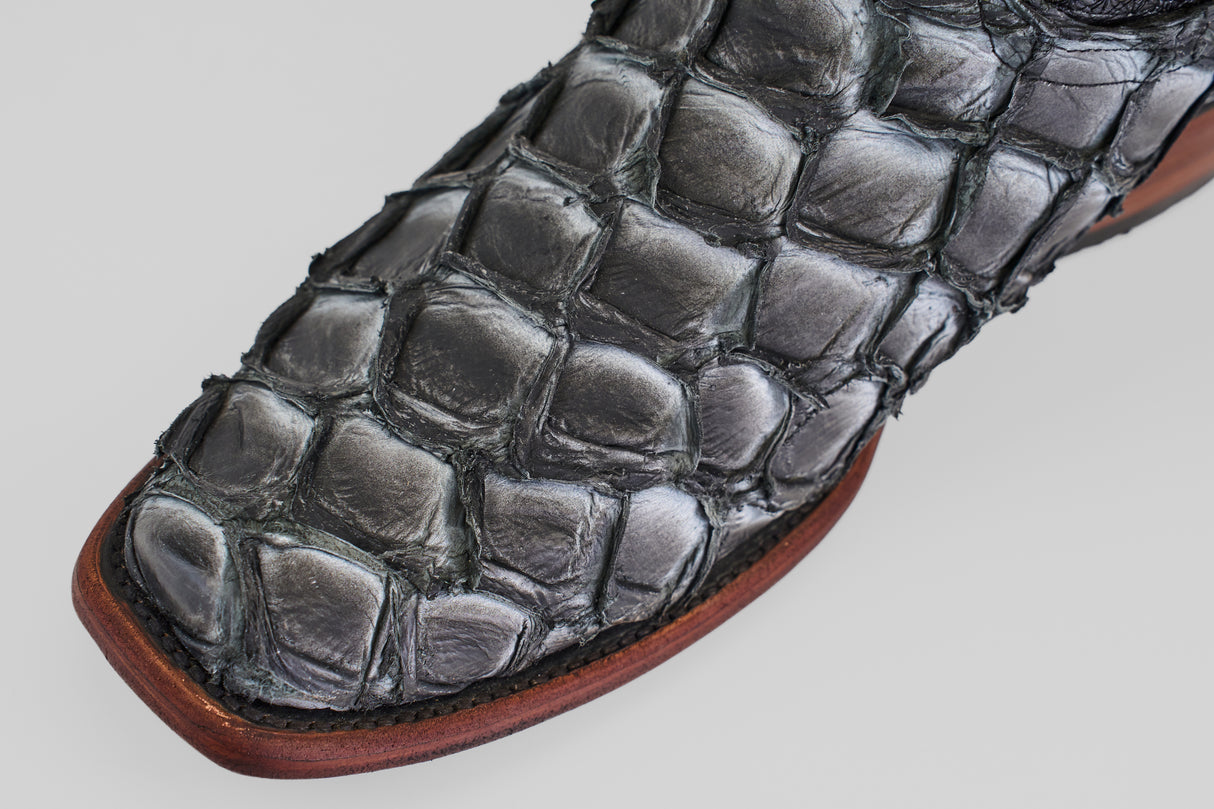 Close-up of the Conor - Newspaper shoe featuring a black, narrow square toe with a crocodile-textured pattern and a brown leather sole, set against a light gray background.