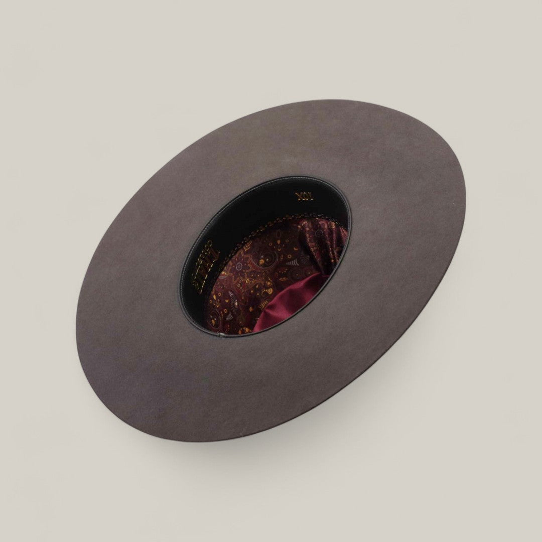 The 10X - Oxford - TC Hat is displayed upside down, featuring a wide gray brim, a black inner band, and a maroon paisley-patterned lining with a shiny accent, set against a plain beige background.