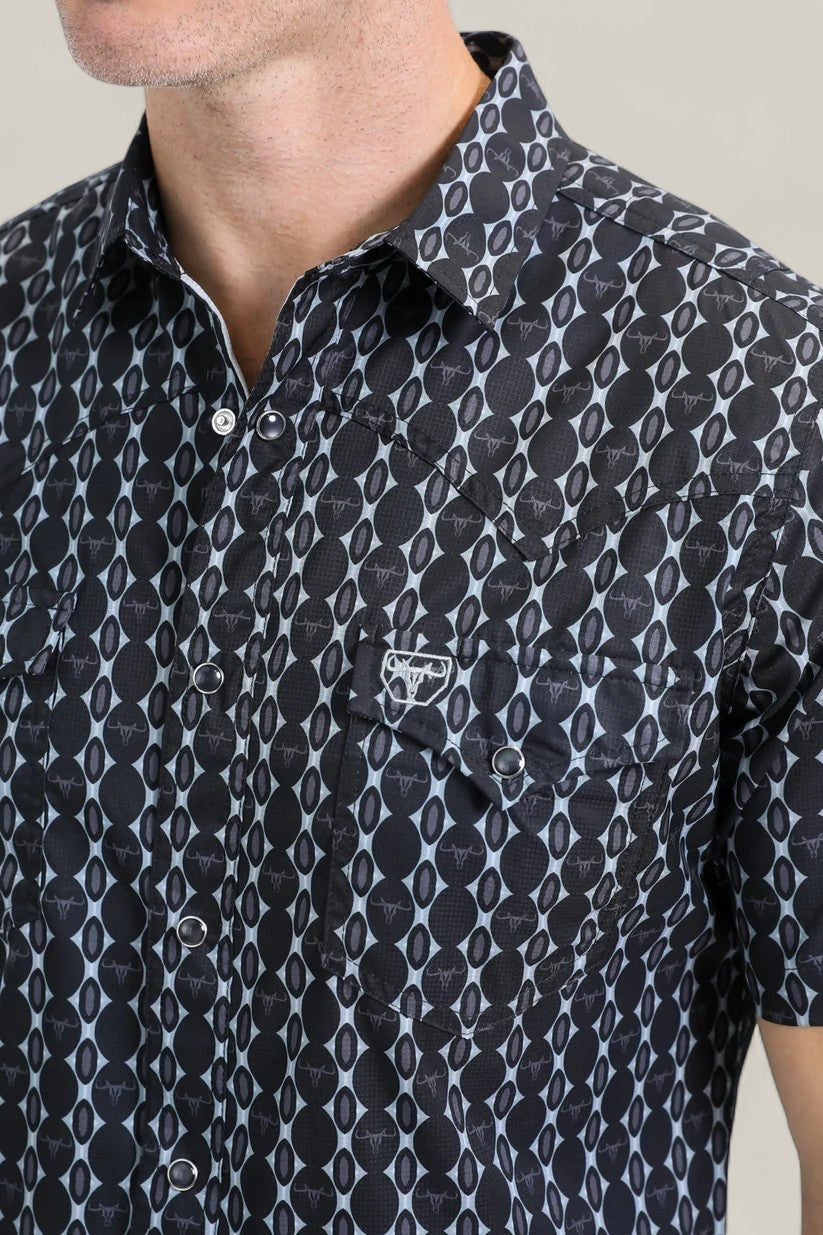 A man is shown from the lower face to upper torso wearing the Mens Performance Western Short Sleeve Aztec Print Navy Shirt - PGW10646, featuring a black and gray geometric pattern and a small embroidered white logo on the chest pocket.