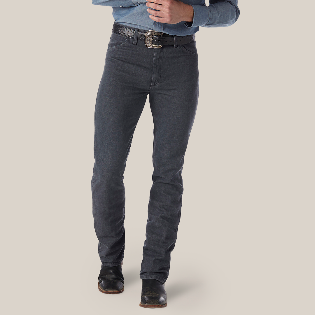 A person sports a blue denim shirt tucked into Wrangler Cowboy Cut Slim Fit jeans in charcoal gray, secured with a black belt. The ensemble is completed with black boots, and the photos focus spans from torso to feet against a plain background.