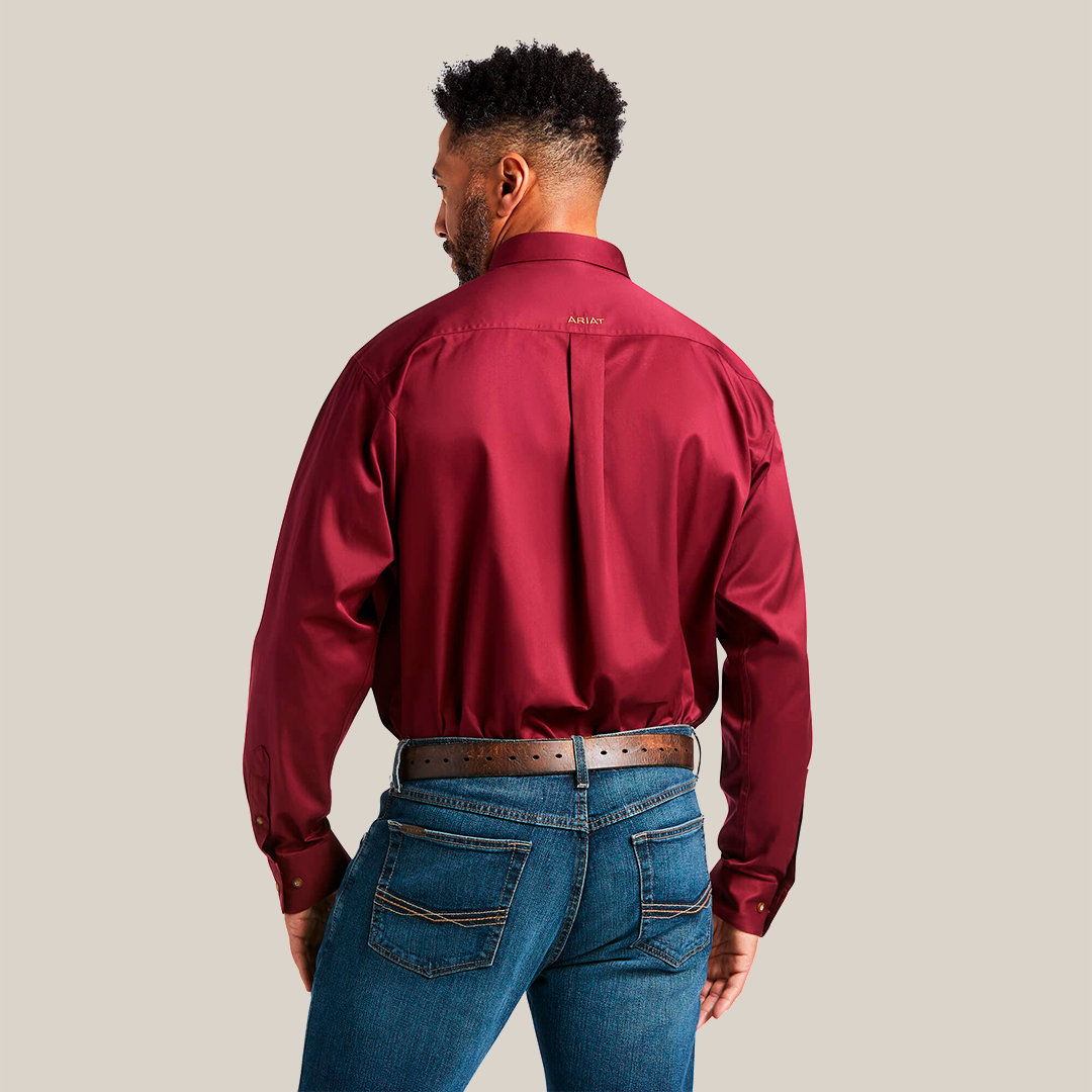 A person with short dark hair and beard, back to the camera, wears a burgundy Solid Twill Classic Fit Shirt (Product: 10012635) tucked into blue jeans along with a belt.