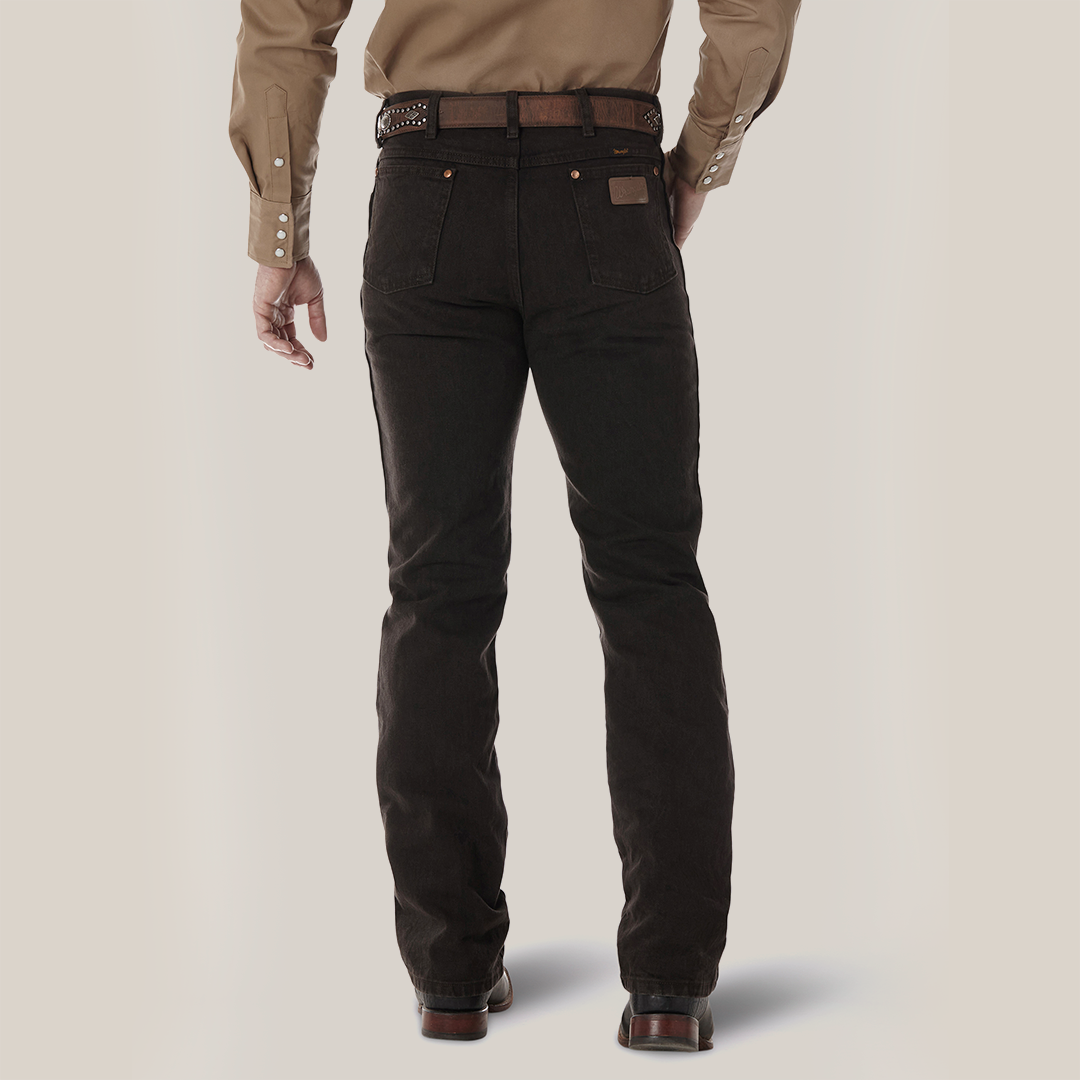 A person seen from the back is wearing a brown long-sleeve shirt and Wrangler Cowboy Cut Slim Fit Jeans (0936KCL) in dark brown with pockets and button details, accessorized with a leather belt. They stand against a light, neutral background.