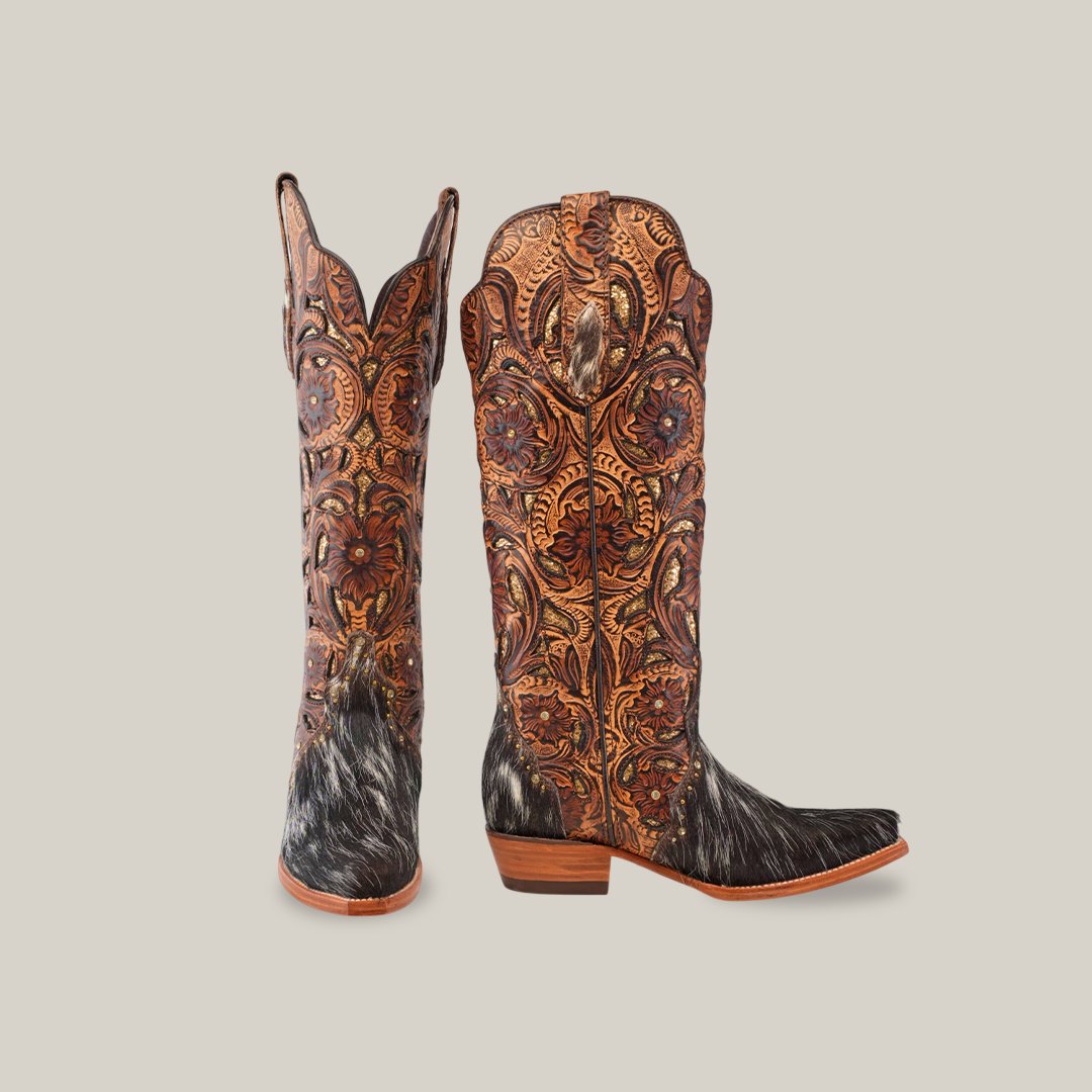 A pair of ornate western boots with intricate leather patterns and dark fur accents on the lower half, set against a plain background.
