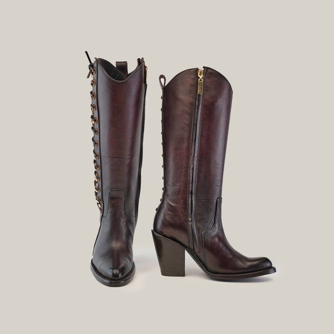 Two brown leather cowboy boots with block heels and sleek design. One boot shows a front view with decorative laces, and the other shows a side view with a visible zipper. Background is light gray.