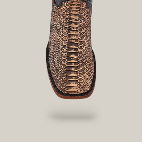 Close-up of the Exotic Python - Rustic Bone boot crafted from python leather, showcasing a textured brown pattern. Featuring a square toe and black trim, it perfectly captures Western appeal against a simple gray background.