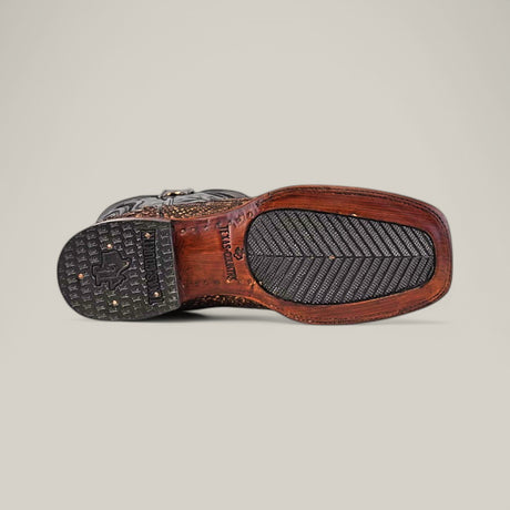 The image features the bottom view of the Exotic Python - Rustic Bone - Square Toe boot, with a textured rubber heel and sole, intricate stitching on python leather, and an engraved brand logo near the arch. Its herringbone-patterned front sole enhances its Western appeal.