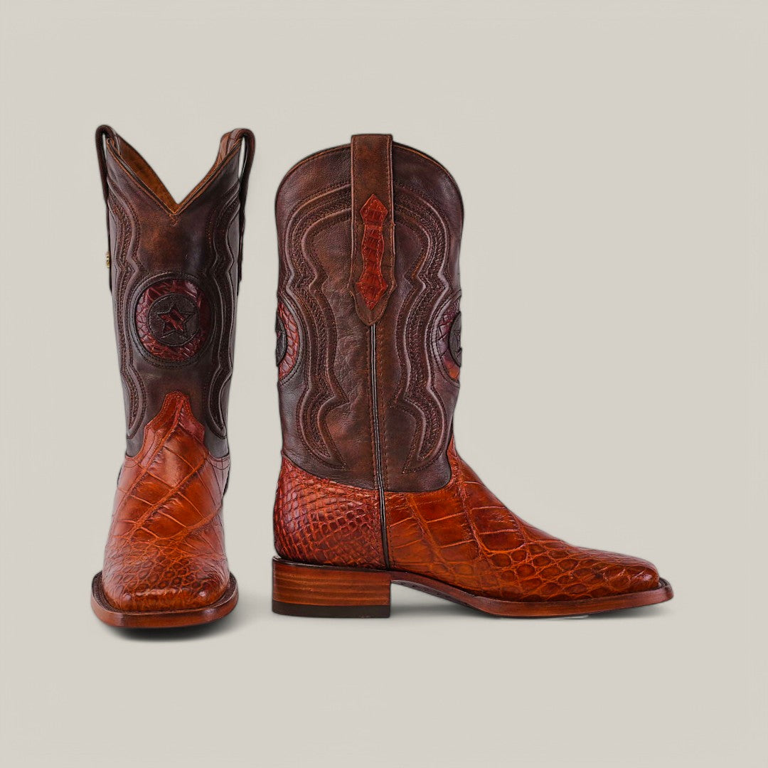 The Exotic American Alligator Hornback boots in Cogñac feature a square toe, intricate brown leather designs, and striking Cognac Alligator Hornback texture. They blend dark and light brown hues with embossed patterns against a plain light gray background.