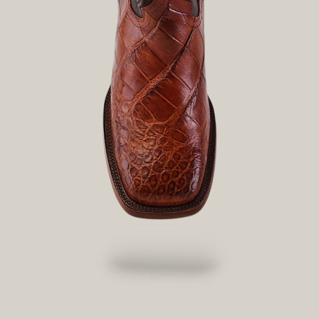 Close-up of an Exotic American Alligator Hornback boot in Cogñac with a square toe, highlighting its detailed textured pattern against a light beige background.