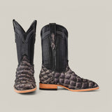 A pair of Exotic Pirarucu Fish - Gray - Square Toe cowboy boots features black leather uppers and textured pirarucu fish leather, placed on a plain background with one boot facing forward and the other angled sideways.