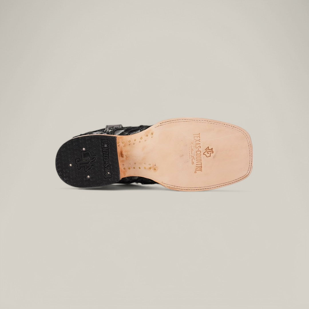 The Exotic Pirarucu Fish - Newspaper - Square Toe cowboy boot features a tan leather sole with branding and decorative stitching, a black heel adorned with metal studs, all set against a plain, light background.