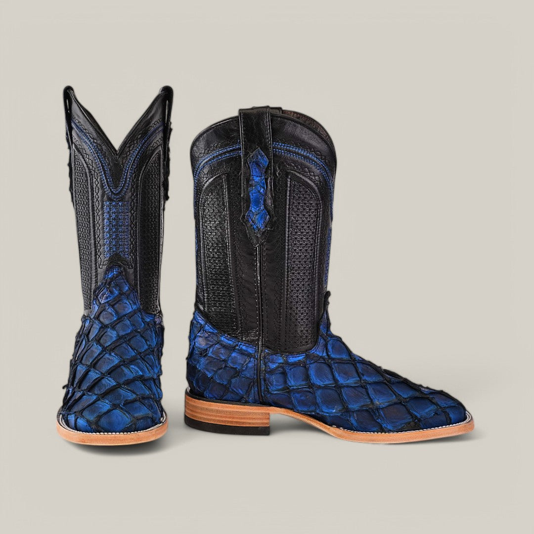 A pair of Exotic Pirarucu Fish cowboy boots in textured dark blue leather, featuring intricate stitching for exotic elegance. The boots have wooden heels and soles, with one upright and the other tilted forward to highlight the unique blue square toe design.