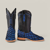 A pair of Exotic Pirarucu Fish cowboy boots in textured dark blue leather, featuring intricate stitching for exotic elegance. The boots have wooden heels and soles, with one upright and the other tilted forward to highlight the unique blue square toe design.