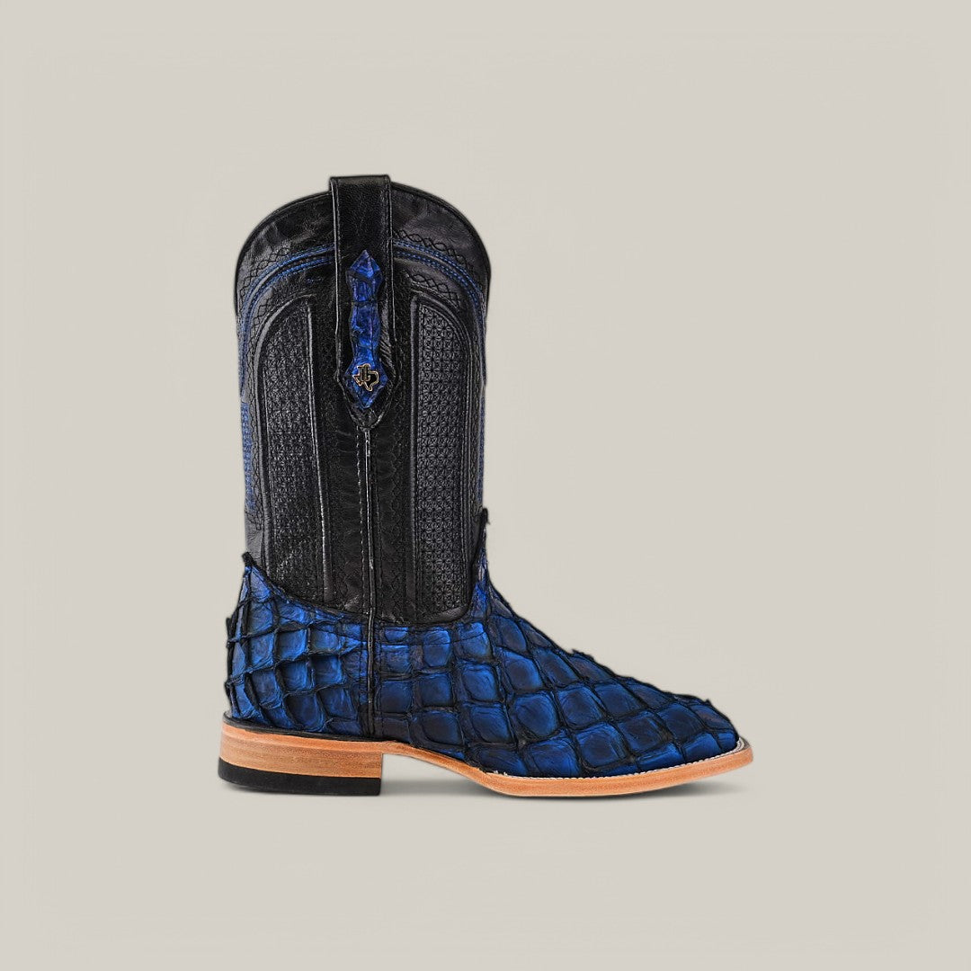 The Exotic Pirarucu Fish - Dark Blue - Square Toe Boot features a black upper and blue textured lower section like Pirarucu fish scales, with a wooden heel and decorative stitching. Its side pull tabs add exotic elegance against a plain background.
