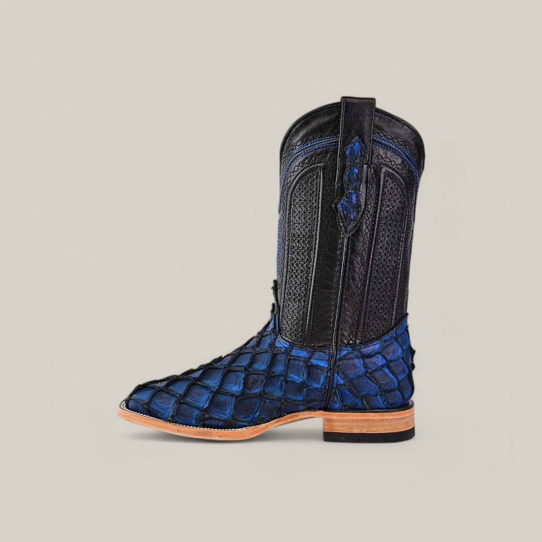 The Exotic Pirarucu Fish cowboy boot features an elegant dark blue square toe with an alligator-like pattern and a classic black upper. A leather sole and detailed stitching enhance its exotic elegance, set against a subtle background.