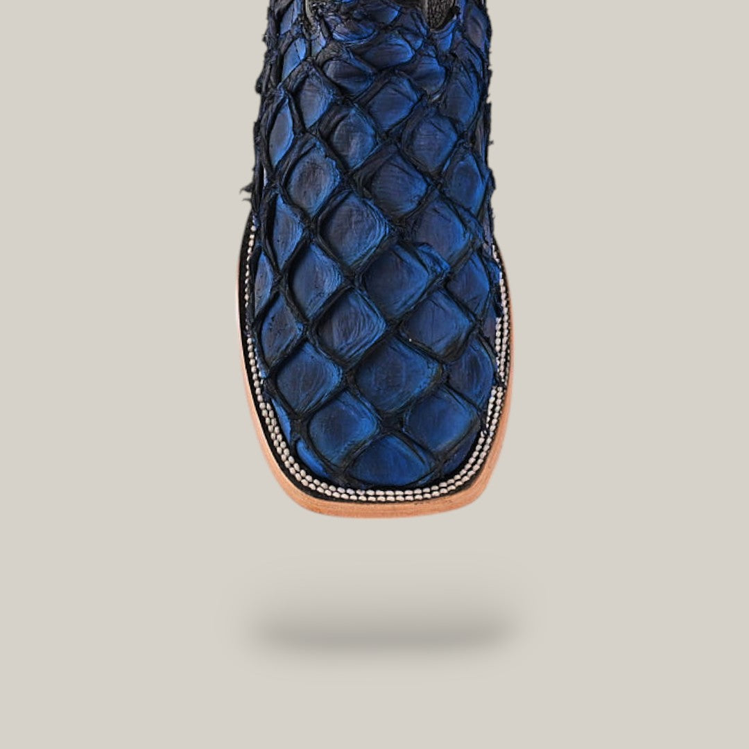 The Exotic Pirarucu Fish-inspired boot features a dark blue and black scaly texture with exotic elegance, while the Blue Square Toe Boot has a light brown sole decorated with stitching along the edge.