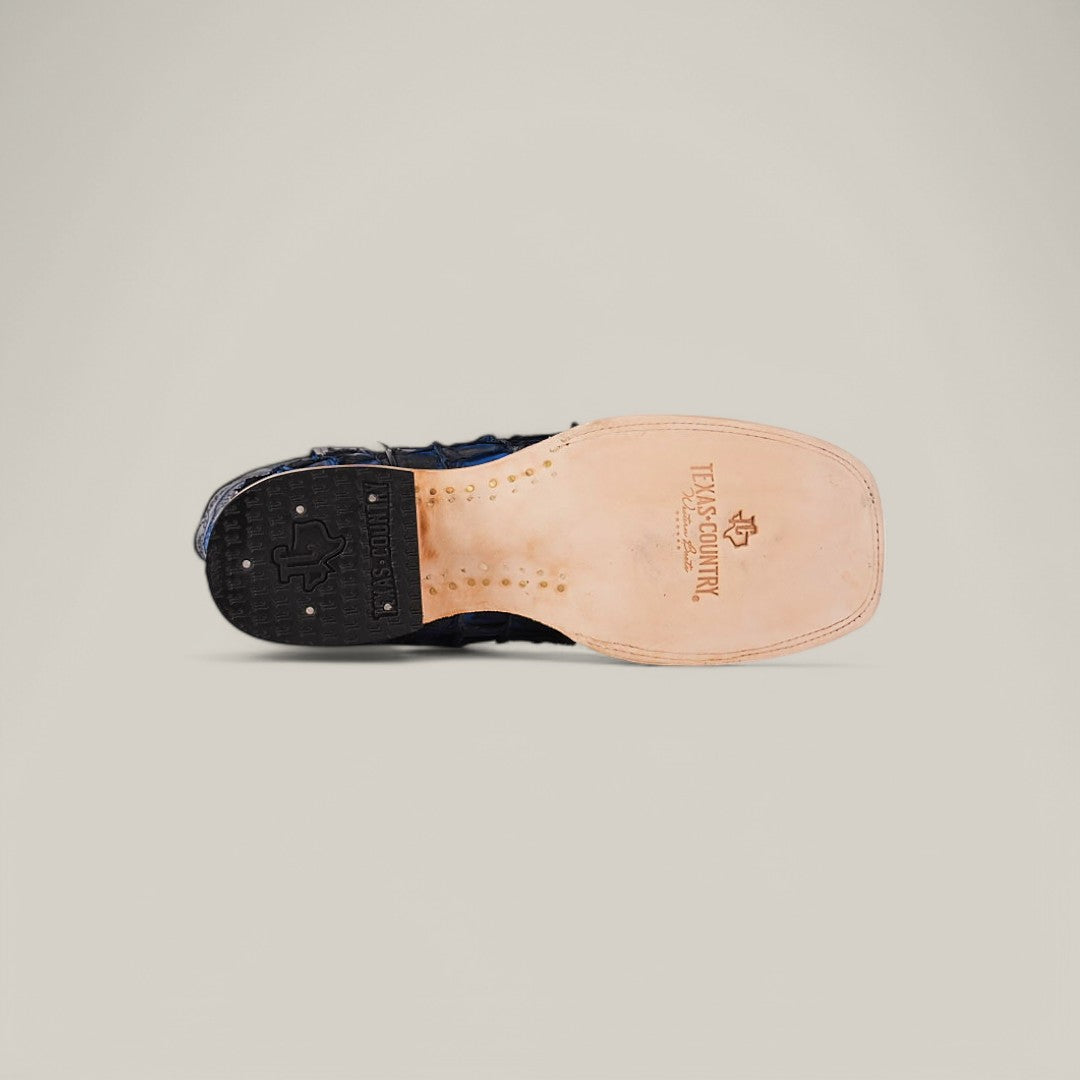 The image displays the sole of an Exotic Pirarucu Fish - Dark Blue Square Toe Boot. Made from light tan leather, it showcases the Texas Outlaw brand and logo. The black heel with small treads offers grip, blending style and exotic elegance beautifully.
