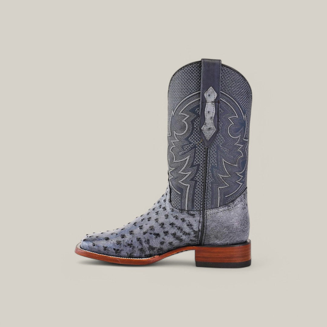 The Exotic Full Quilt Ostrich - Safari Gray - Square Toe boot showcases a textured pattern in a rich gray shade with decorative stitching, paired with a brown wooden heel, all set against a plain light backdrop.