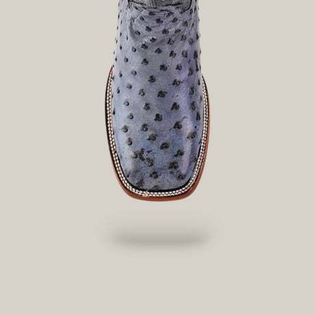 A close-up of the Exotic Full Quilt Ostrich - Safari Gray cowboy boot features a square toe and decorative stitching, set against a plain pale background.