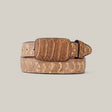 The Python Print Cappuccino Belt features a Texas buckle and showcases embossed patterns that mimic scales and ridges for a python print design. Crafted from premium brown leather, its elegantly displayed coiled with the buckle forward on a plain light background.