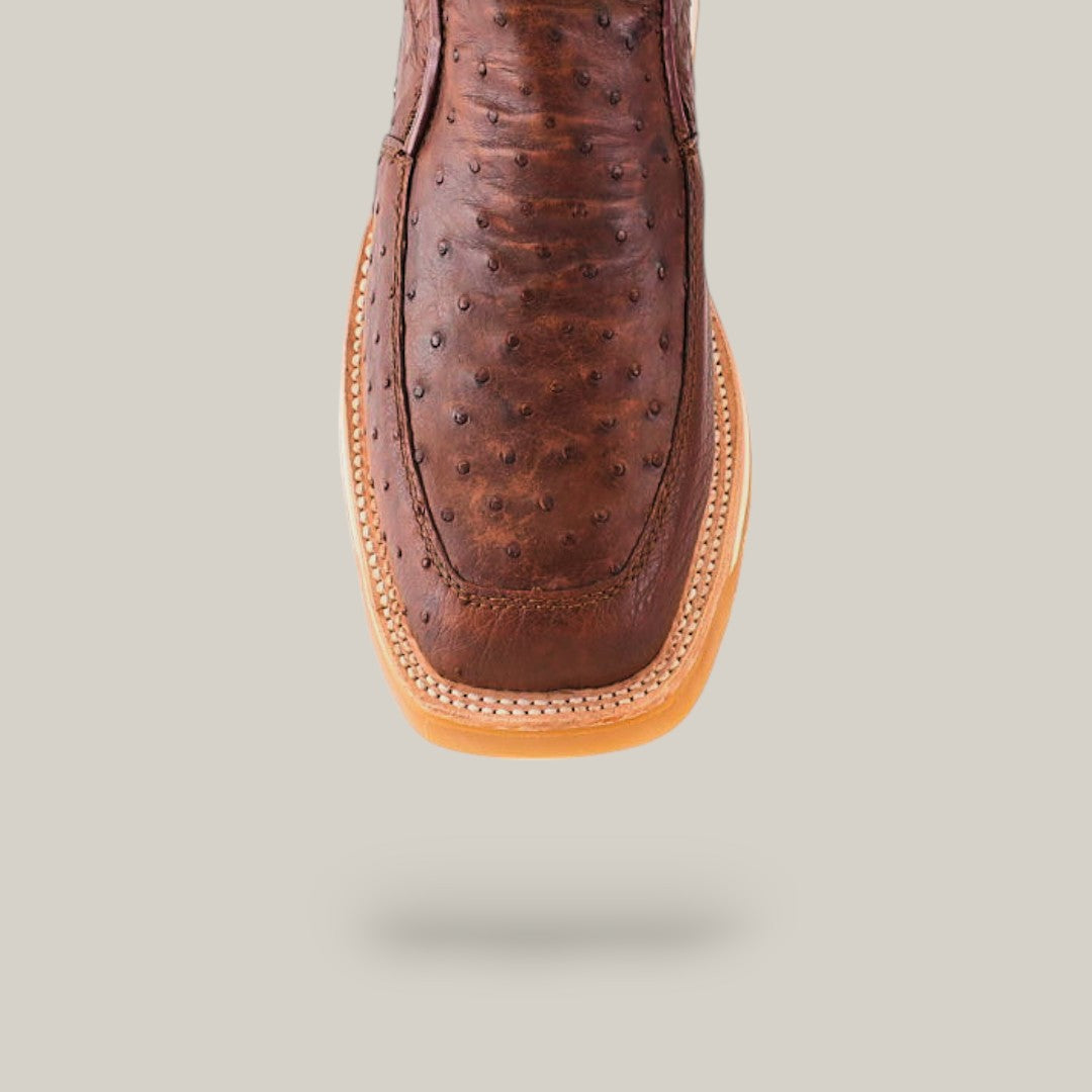 Close-up of the Exotic Ostrich - Mink - Ankle Boot, a luxury brown leather cowboy boot made from ostrich leather with a square toe. Set on a plain beige background, the intricate detailing and craftsmanship are elegantly highlighted.