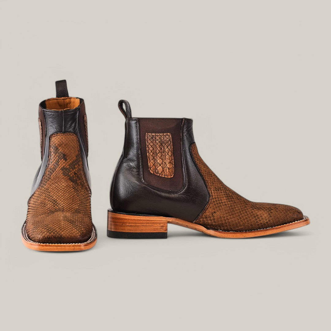 The Exotic Python - Tamarindo ankle boots are stylish Chelsea boots in brown, featuring a python-embossed leather texture, dark elastic side panels, and light brown wooden soles set against a plain gray background.
