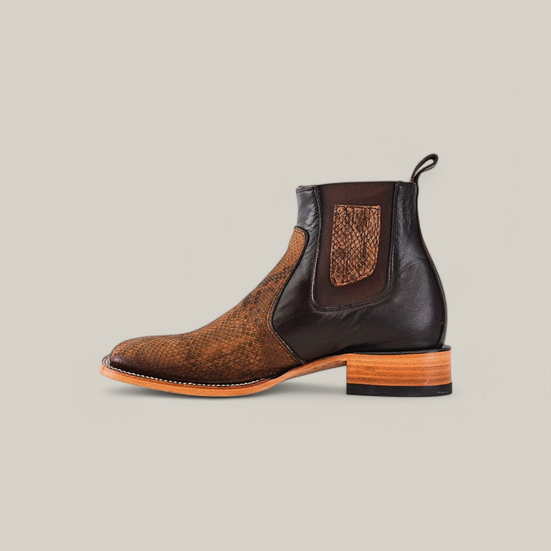 The Exotic Python - Tamarindo Ankle Boot is a sophisticated choice in brown and black, featuring a Python-embossed leather, side elastic panel, and wooden heel, elegantly displayed on a plain beige background.