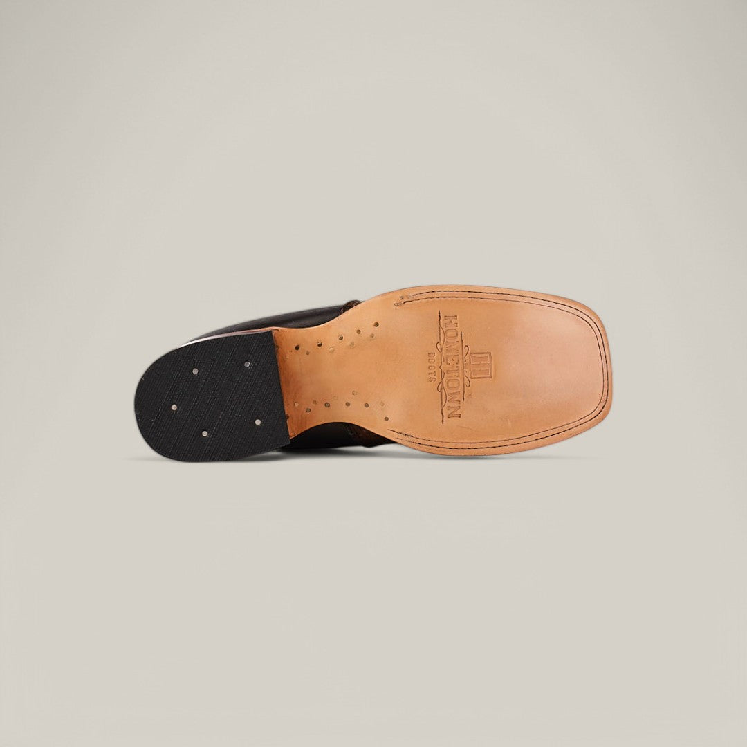 The image displays the Exotic Python - Tamarindo ankle boots underside, featuring a tan leather sole and black heel. This elegant boot includes decorative stitching, brand embossing, and metal elements on the heel against a plain gray background.