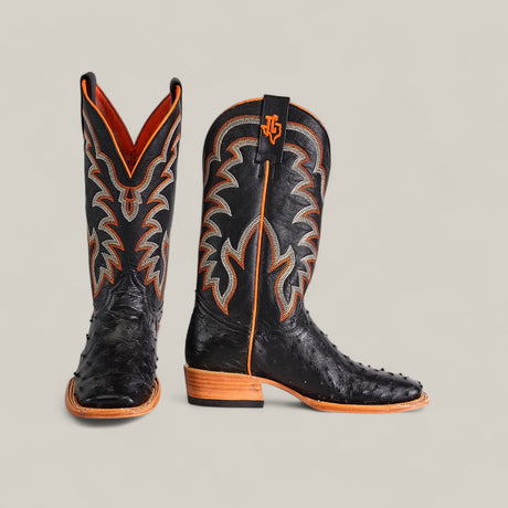 A pair of Exotic Full Quilt Ostrich - Black - Square Toe cowboy boots with orange and gray stitching, a wooden heel, and textured ostrich leather. One boot stands upright; the other is angled to show the side.