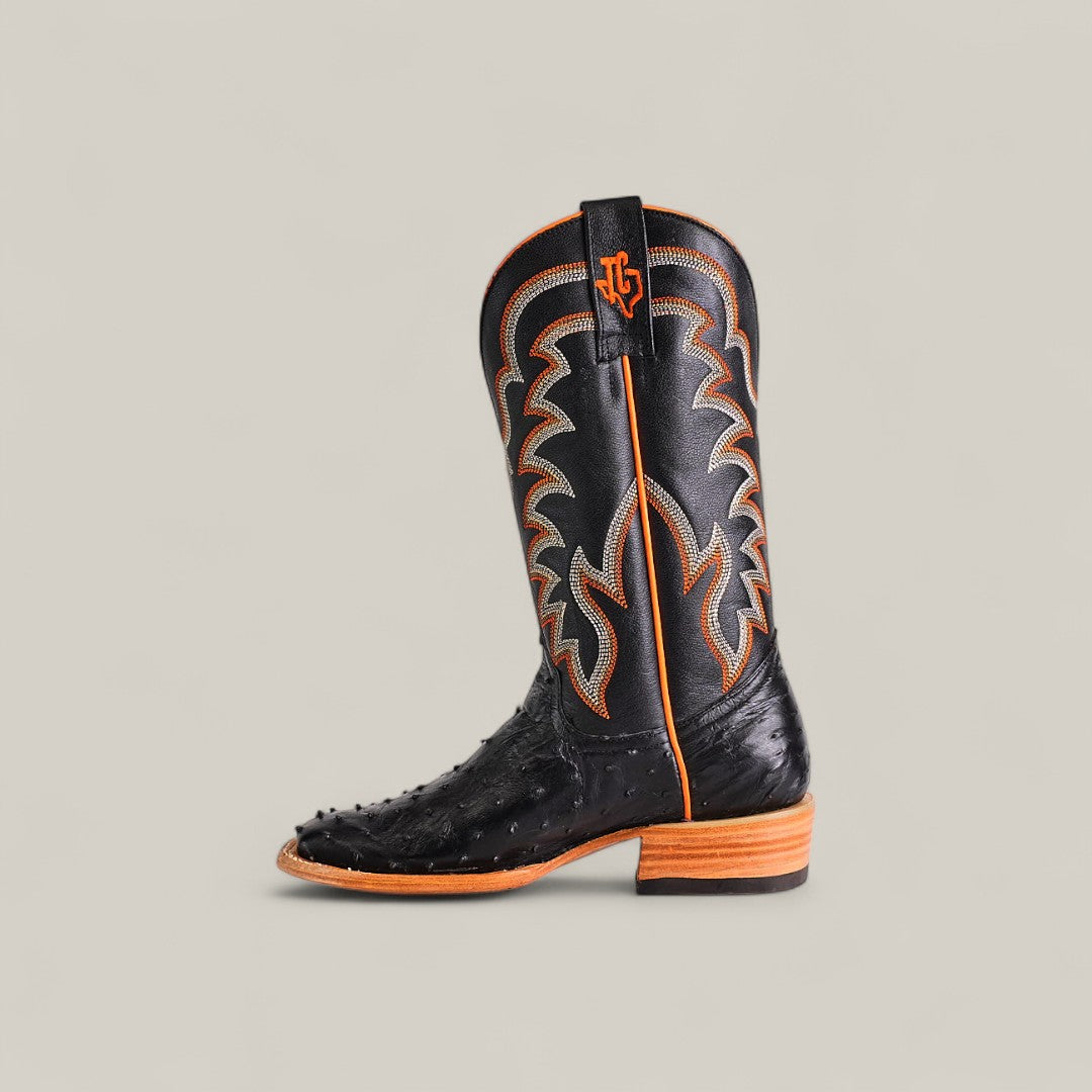 The Exotic Full Quilt Ostrich - Black - Square Toe boot features black ostrich leather, orange and gray stitching, a wooden sole, and embossed texture, showcased against a plain light gray background.