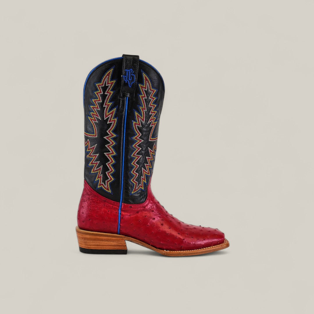 A single Exotic Full Quilt Ostrich - Red - Square Toe cowboy boot with a red ostrich leather foot, black shaft with multicolored zigzag stitching, blue piping, and stacked wooden heel is displayed on a plain beige background.