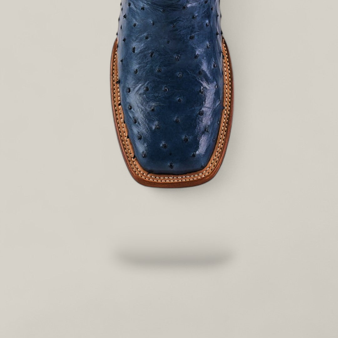 Top view of the Exotic Full Quilt Ostrich - Blue - Square Toe boot, highlighting its stylish square toe and tan welt stitching on a light gray background. The blue ostrich boot casts a soft shadow below.