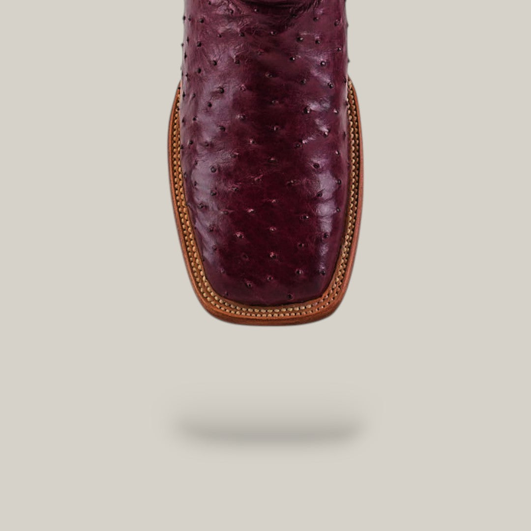 A close-up of the Exotic Full Quilt Ostrich - Wine - Square Toe boot highlights its rich wine-colored ostrich leather, sophisticated square toe, and brown stitched welt, set against a plain light gray background with a subtle shadow.