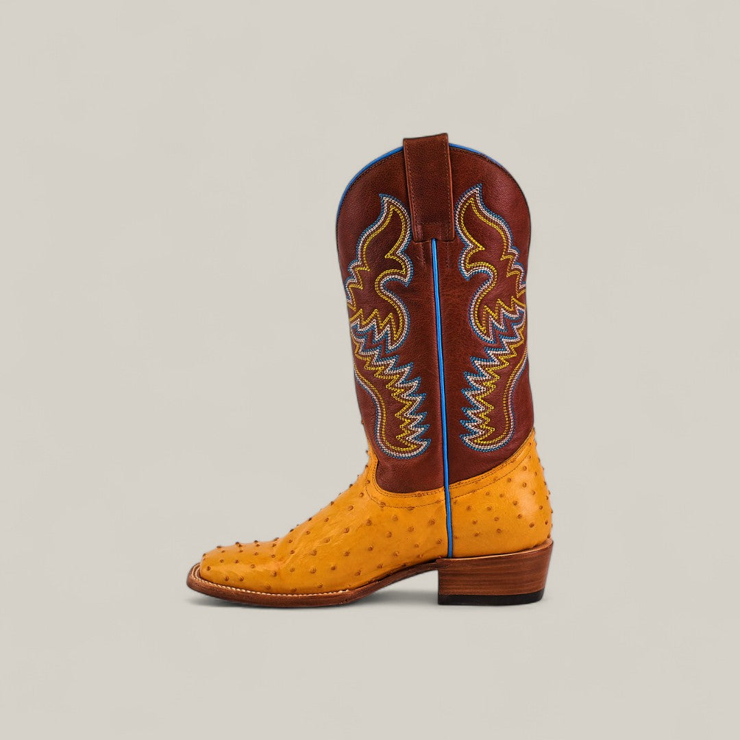 The Exotic Full Quilt Ostrich - Buttercup - Square Toe boot from the Platinum Collection features a textured yellow-tan ostrich leather foot, brown shaft with yellow and blue stitching, blue piping and pull strap, and a low wooden heel. Shown in profile.