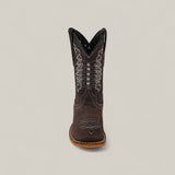 The Orion Suede Oxford - Square Toe Kids Boot is shown from the front in brown suede, featuring intricate white and silver stitching with decorative patterns, set against a plain light gray background.