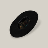 The 25X Grizzly - Black - TC Hat is a wide-brimmed luxury black hat with a decorative patterned inner band, shown from above on a plain beige background.