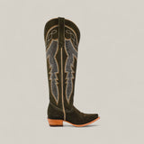The Della Olive Green boot features a tall shaft, snip toe, decorative stitching on olive green leather, and a low wooden heel, shown against a plain beige background.